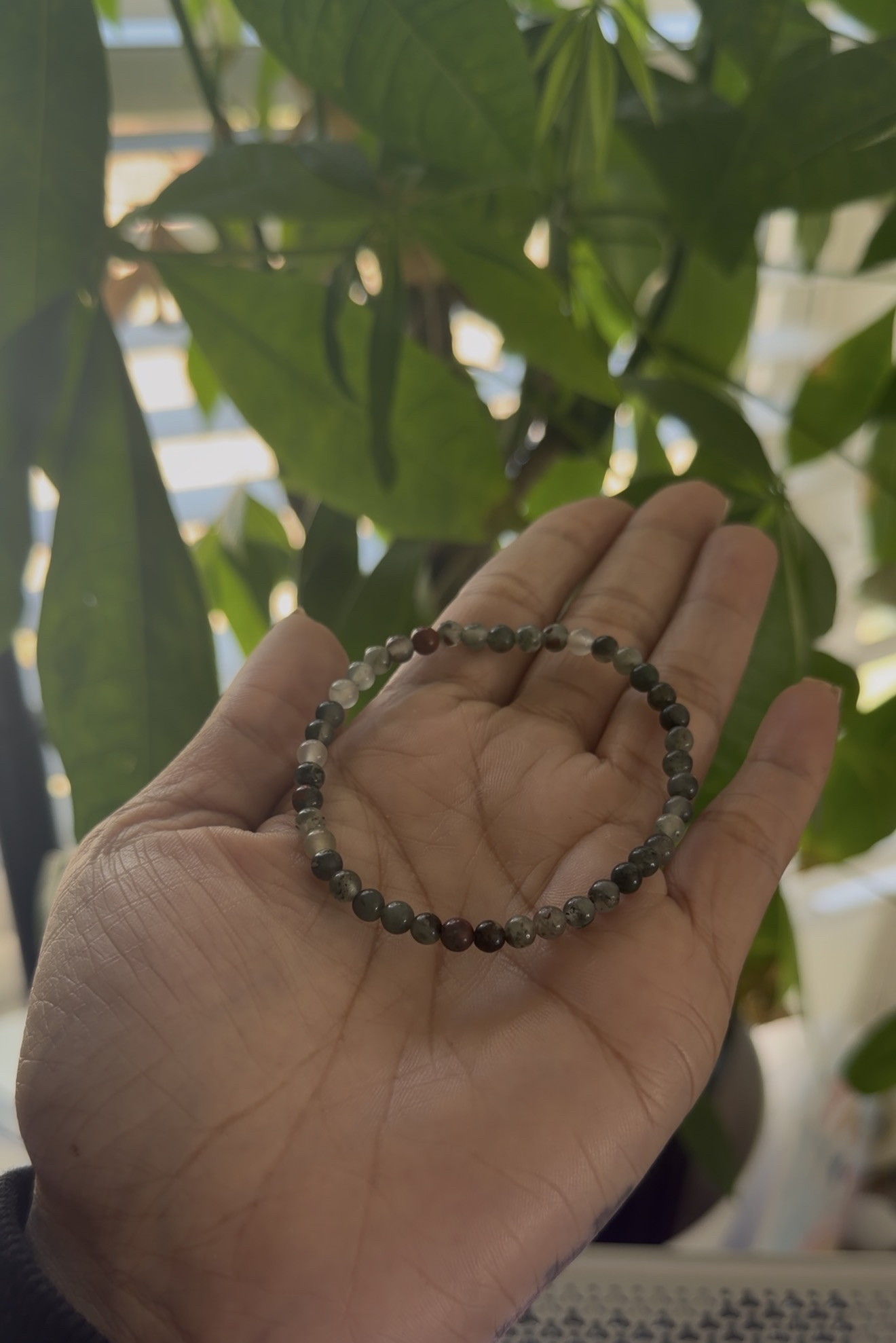 Hand holding a beaded bracelet with green leaves in the background